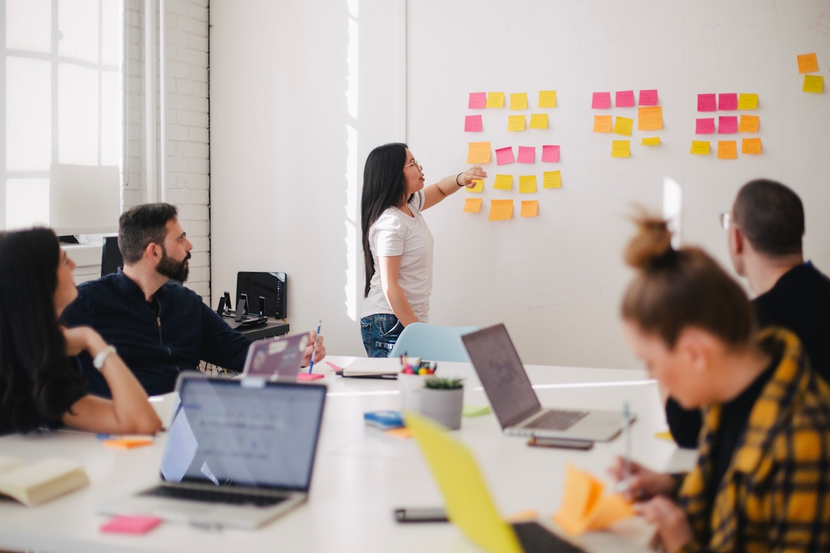 Woman presenting with sticky notes on a wall to a small team in a bright office